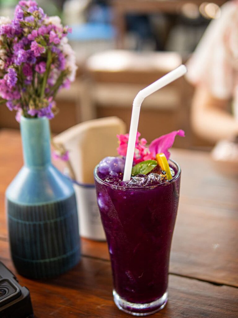 Glass of purple fruit drink with ice and flowers